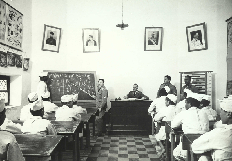 Interiors of a juvenile school. The image shows a classroom during a lesson. Portraits of famous Italian figures are hanged on the wall, among whom, H.E. Benito Mussolini is recognizable.1923 - 1945