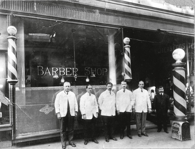 A team of barbers pose outside their shop, early twentieth century . Various signs, including those on the barber poles, advertise manicures, massage, and shoeshines, in addition to hair cuts. (Photo by Vintage Images/Getty Images)